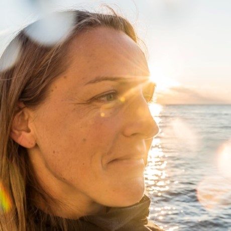 A stock photograph of a woman by the seaside with sunlight beaming behind her.