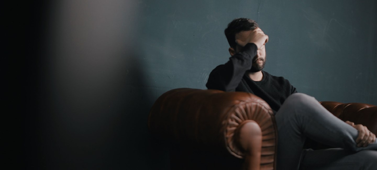 Person sitting on an armchair, touching his head.