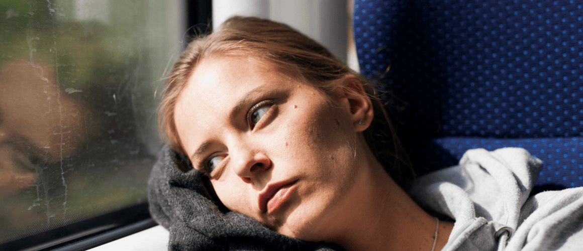 Woman sitting on a train, leaning her head against the window while staring outside.