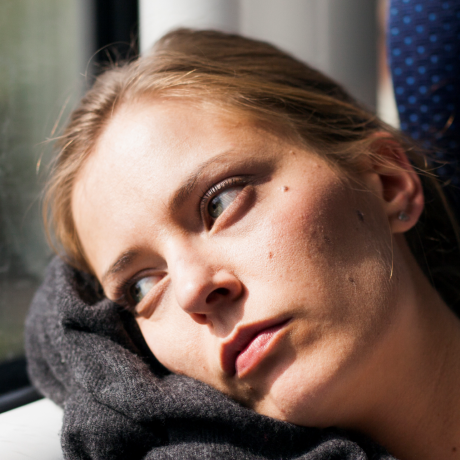 Woman sitting on a train, leaning her head against the window while staring outside. 