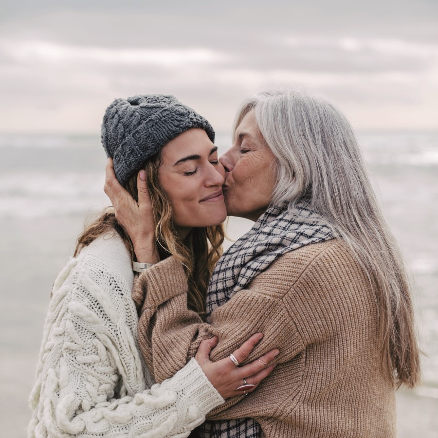 Two women, one older and one younger, embracing each other on a beach.