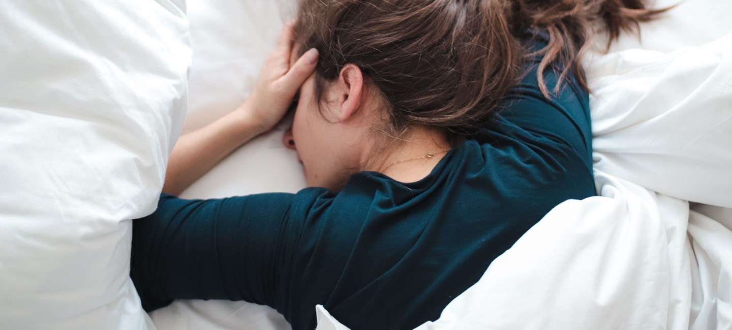 Woman lying in bed on her stomach while holding head.