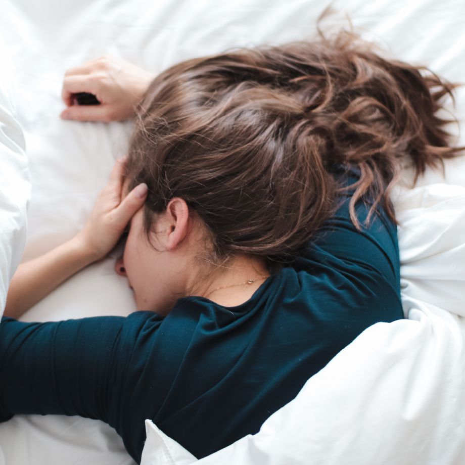 Woman lying in bed on her stomach while holding head.