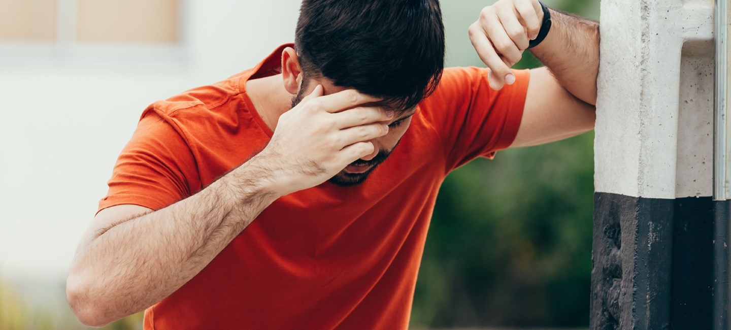 Stock photo of a person leaning against a wall, touching their head.