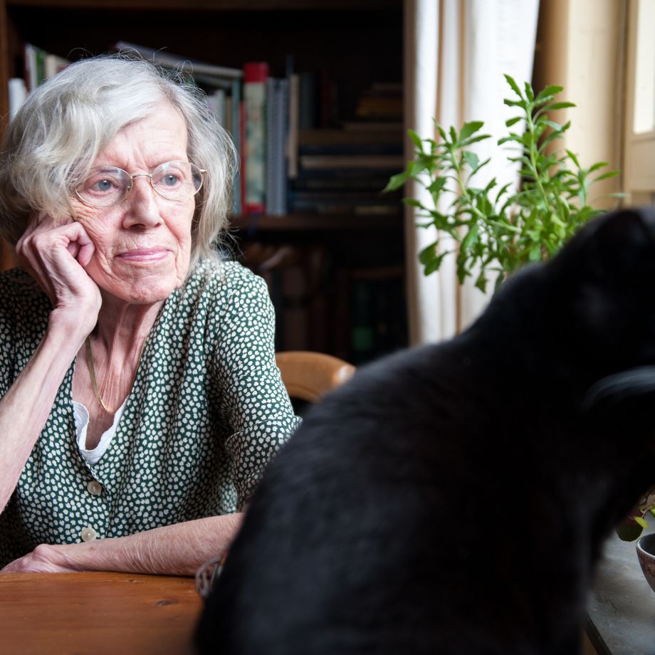 LADY OF ADVANCED YEARS, SITTING AT TABLE WITH CAT, LOOKING UNHAPPY